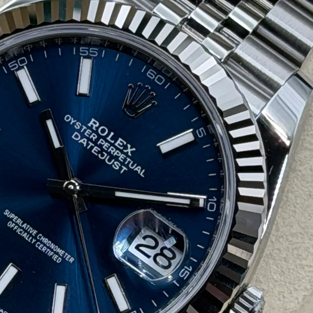 Makroaufnahme einer Rolex Datejust 41 aus unserem Bestand: blaues Zifferblatt mit Rolex-Krone und Beschriftung, Rehaut mit Gravur, geriffelte Lünette und Gehäuse